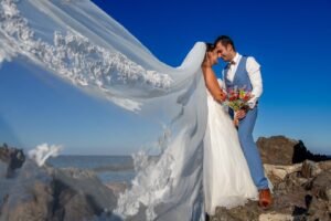 Mariés photographiés au bord de la mer près de Perpignan - Mariage en montagne dans les Pyrénées-Orientales : couple de mariés enlacés sur un sommet, voile au vent.