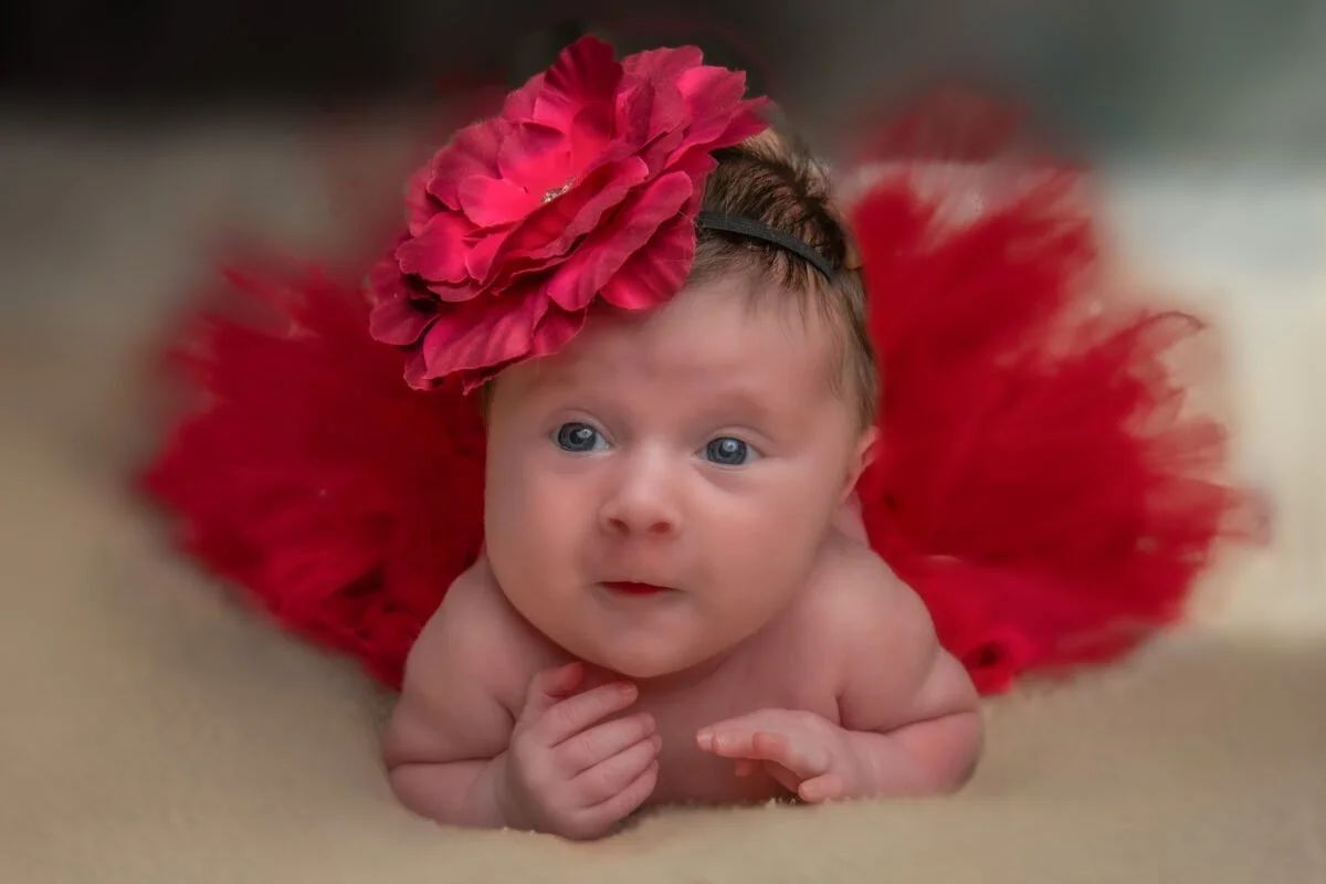 Bébé éveillé, allongé sur le ventre, portant un bandeau fleuri rouge assorti à une jupe en tulle.