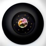 Plat gastronomique minimaliste au centre d’une grande assiette noire.