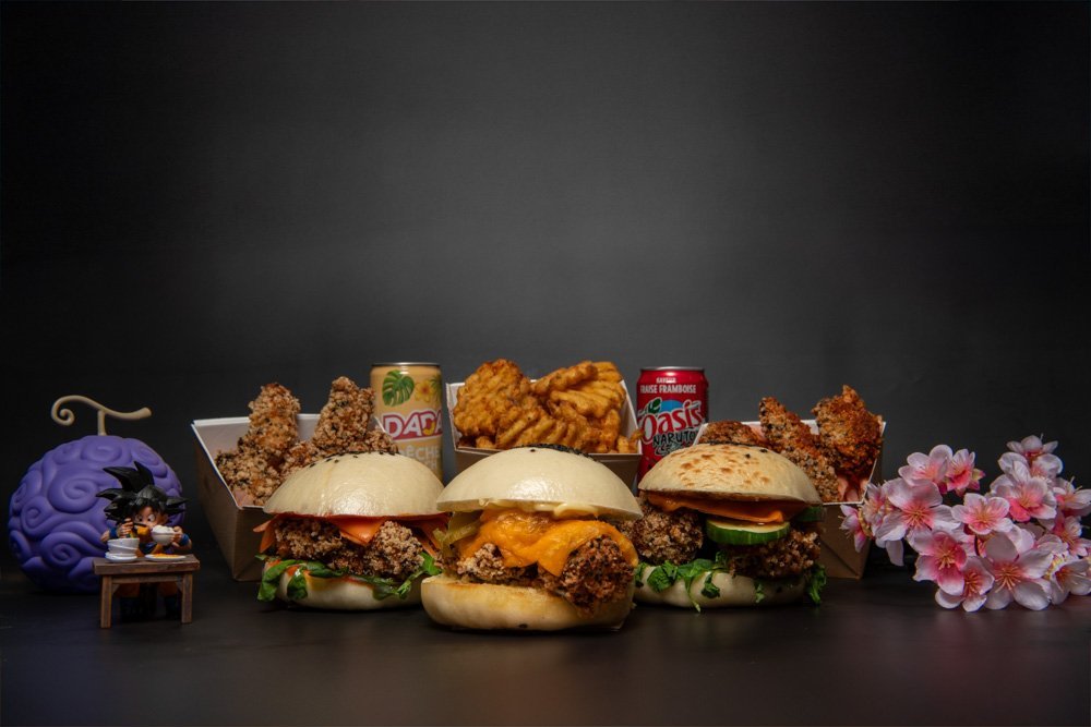 Trio de burgers au poulet croustillant, frites gaufrées, boissons japonaises et décoration manga sur fond noir.