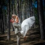 Marié en tenue militaire soulève sa mariée dans une forêt de pins, instant romantique et complice.