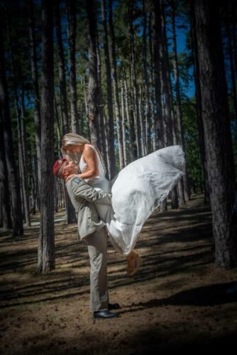 Marié en tenue militaire soulève sa mariée dans une forêt de pins, instant romantique et complice.