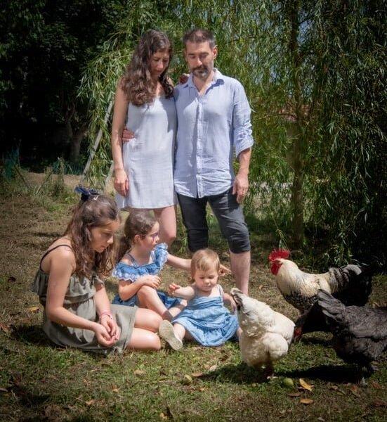 Photographe famille 66 – Enfants jouant dans l’herbe avec poules et coq, ambiance champêtre