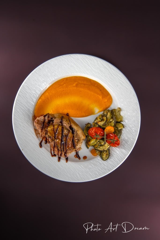 Assiette gastronomique composée d’une viande nappée de sauce balsamique, d’une purée de potimarron et de légumes rôtis.