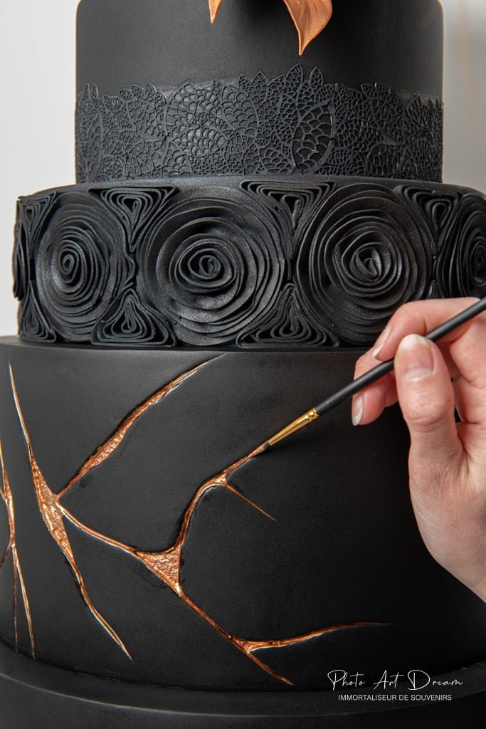 Gâteau noir décoré à la main avec des motifs floraux et des craquelures dorées façon kintsugi.
