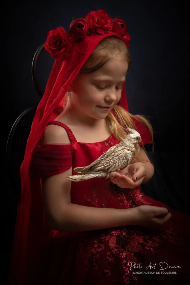 Petite fille en robe rouge tenant un oiseau, portrait artistique en studio