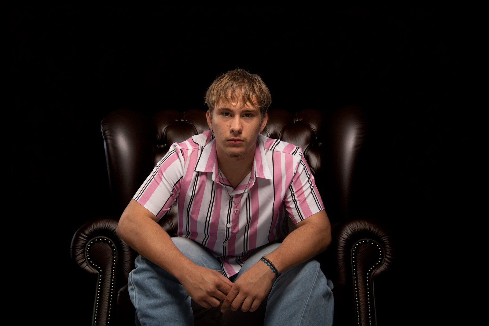 Portrait studio d’un jeune homme assis dans un fauteuil, regard face caméra